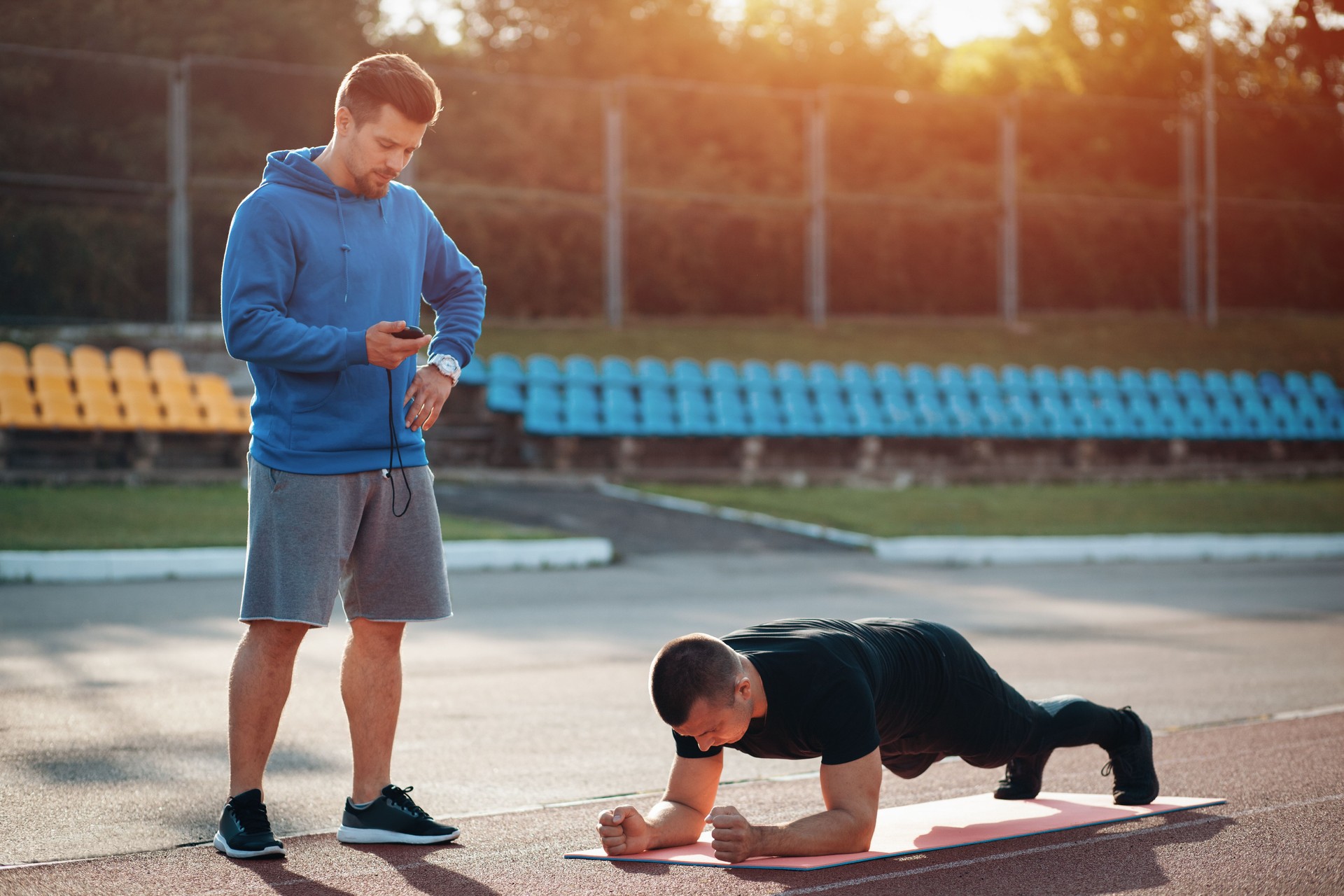 man doing plank exercise and workout with personal fitness trainer outdoor